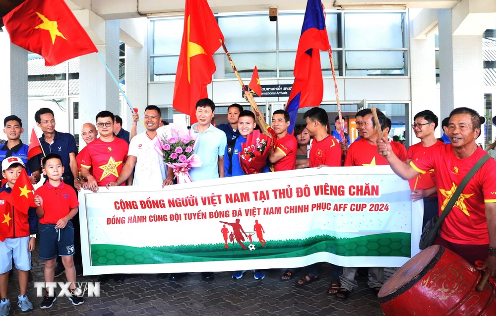 Les supporters vietnamiens au Laos et la communauté vietnamienne au Laos prennent des photos souvenirs avec l'entraîneur Kim Sang-sik et certains joueurs de l'équipe nationale du Vietnam à l'extérieur du hall d'arrivée de l'aéroport international de Wattay. (Photo : Xuan Tu/VNA)