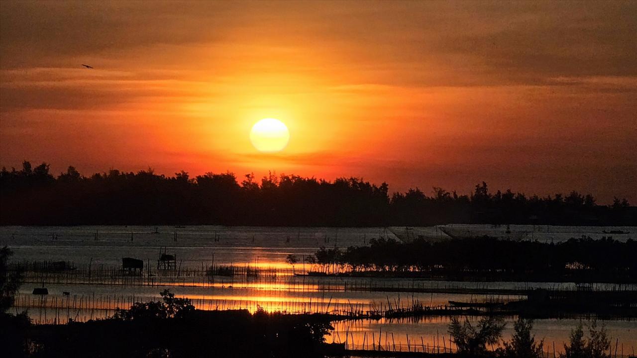 Khoảng 05h10, mặt trời bắt đầu ló ra từ phía phá Tam Giang, hệ đầm phá lớn nhất Đông Nam Á. Những tia nắng bắt đầu len lỏi qua những ngọn cây chá đang thưa lá, kết hợp với một chút sương mờ tạo nên một không gian ảo diệu, đẹp mắt. 