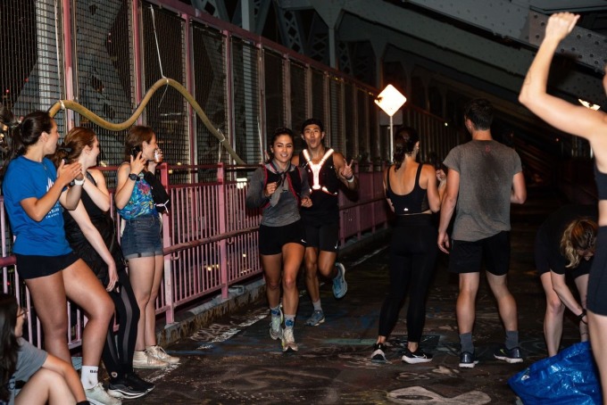 Zwei Läufer laufen während eines spontanen Laufs am Abend des 14. Juli in New York durch einen Anfeuerungsbereich und eine Wasserstation in der Mitte der Williamsburg Bridge. Foto: Runners World