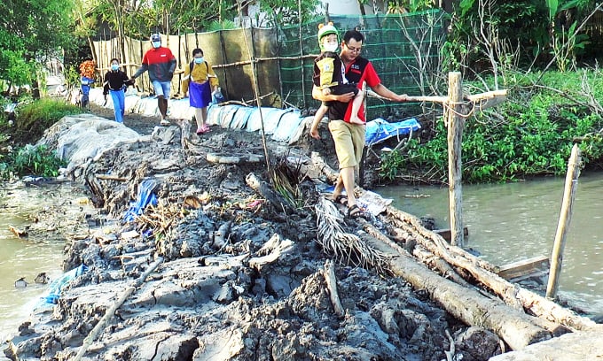 El señor Nguyen Minh Thai lleva a su bebé a través de la carretera temporal en el lugar del deslizamiento de tierra. Foto: An Minh