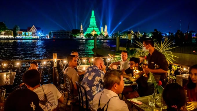 Du khách ăn tối ngoài trời tại một nhà hàng bên bờ sông Chao Phraya, ngắm chùa Wat Arun (thắp đèn màu xanh) ở Bangkok, Thái Lan. Ảnh: AFP