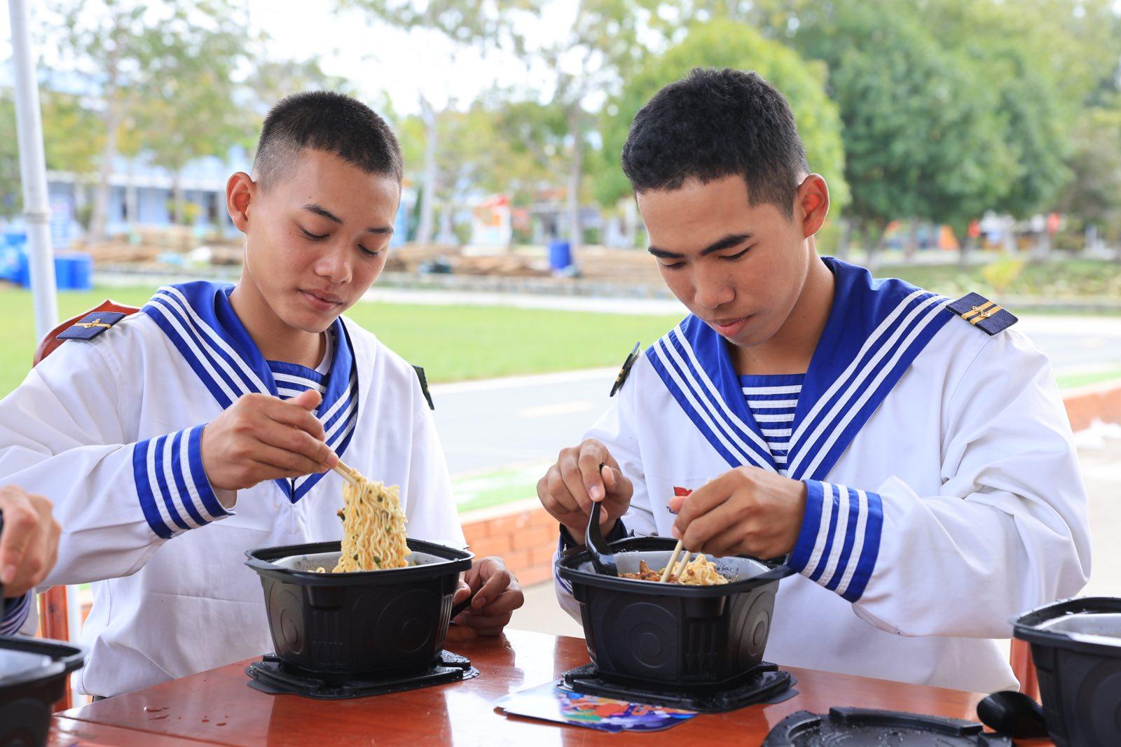 A couple of young men eating noodles Description automatically generated