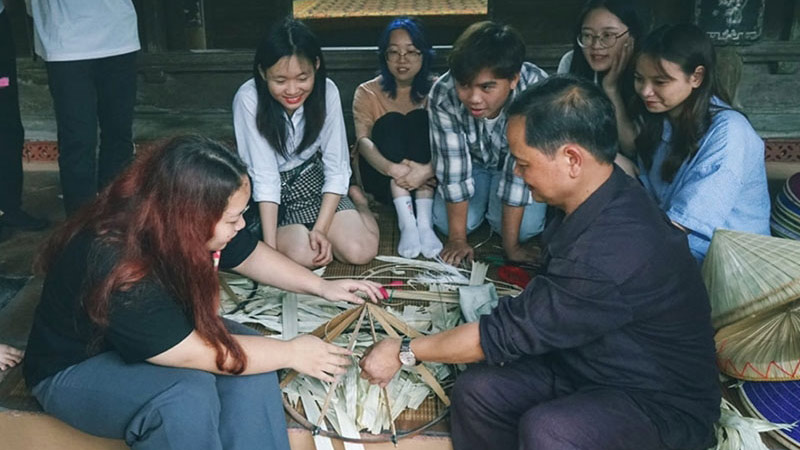 Artisan Le Van Tuy guides a group of young people in weaving conical hats in Chuong village. Photo: QUY DUC
