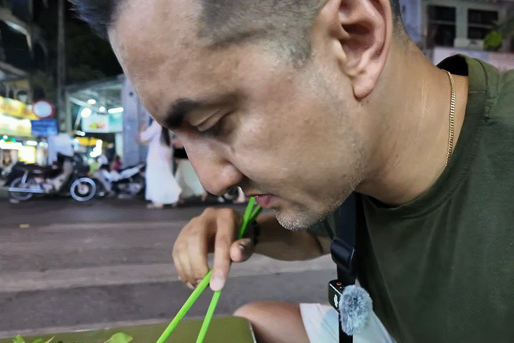A customer sitting on the sidewalk in Hanoi, eating a dish, praised it as 'the best in Vietnam'