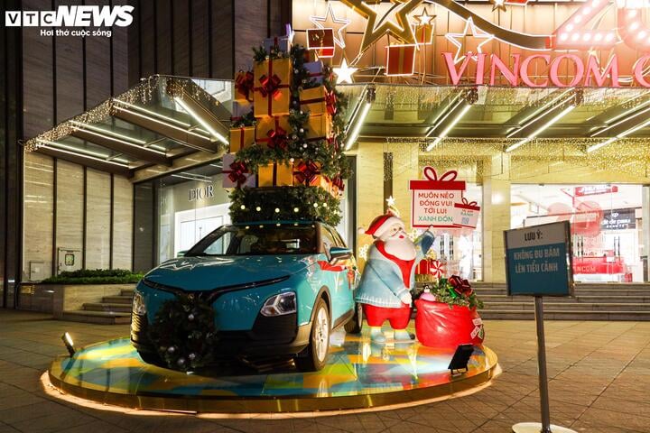 Ein Elektroauto, das mit einer riesigen Geschenkbox auf dem Dach und dem Weihnachtsmann daneben dekoriert ist.