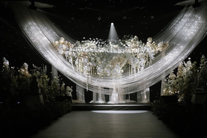 El escenario principal del salón de banquetes es una espléndida pared de flores con muchas luces que crean un espacio brillante y lujoso. Justo en el centro del escenario, los nombres de los novios están colocados de forma destacada en la pared de flores.