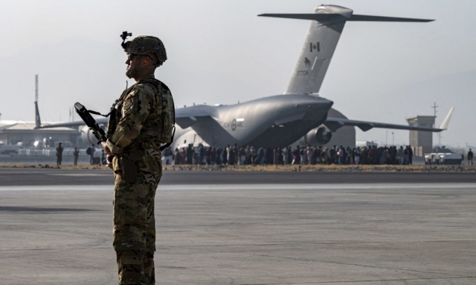 2021年8月20日、アフガニスタンのカブール空港で米兵が警備に当たっており、遠くにC-17軍用輸送機への搭乗待ちの列が見える。写真：AFP