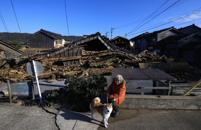 A woman and her dog sit in front of a house that collapsed after an earthquake in Wajima city. Photo: AFP