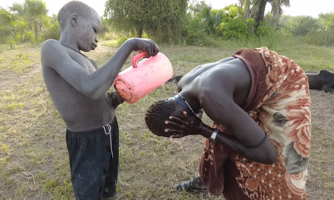 Two Mundari people bathe in cow urine contained in plastic cans. Photo: Lai Nguu Chan