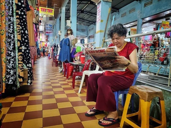 พ่อค้าแม่ค้ารายย่อยในตลาดที่ใหญ่ที่สุดในเมืองวิญลองอ่านหนังสือพิมพ์ทั้งวันและเก็บของในตอนกลางคืน