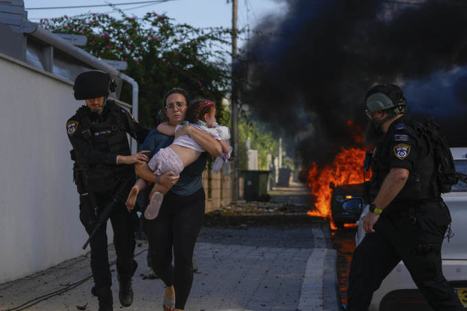 イスラエル警察は、10月7日、イスラエル南部アシュケロンで、ガザ地区からのロケット弾攻撃を受けた地域から逃げる娘を抱えた女性を支援する。写真：AP