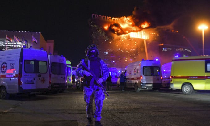 Des gardes nationaux russes maintiennent la sécurité à l'extérieur du bâtiment Crocus, dans la banlieue de Moscou, dans la nuit du 22 mars, alors que les étages supérieurs brûlent violemment. Photo : AP