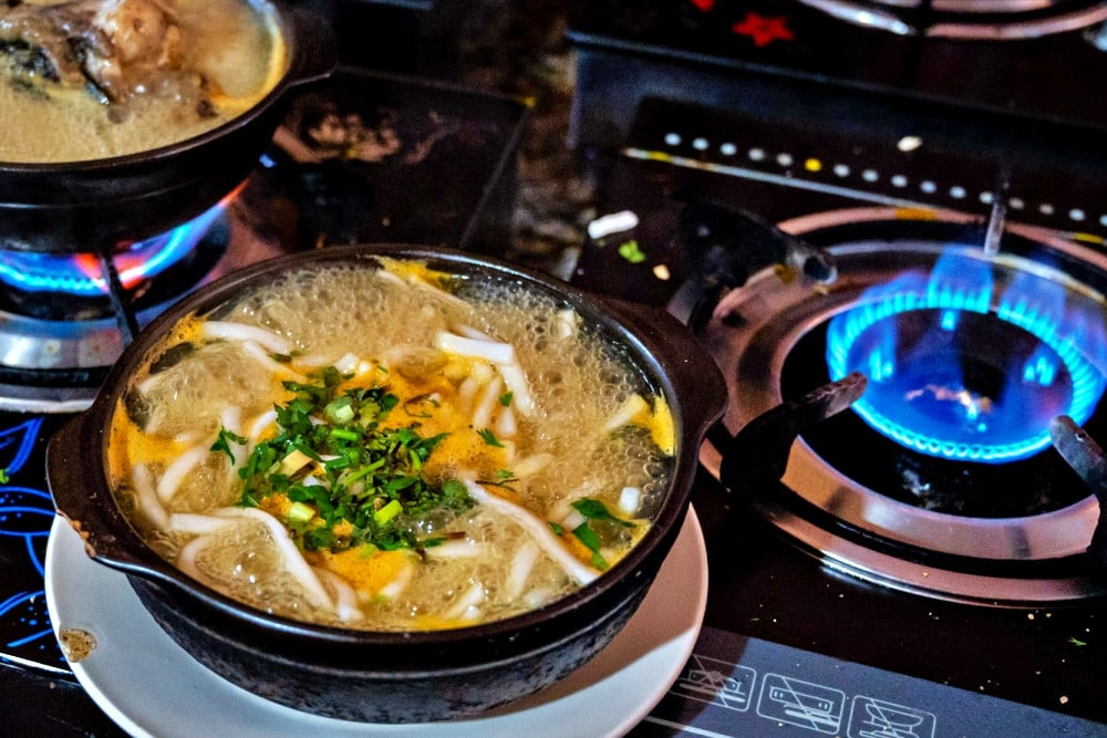 La sopa de fideos con pez cabeza de serpiente se hierve en una olla y los clientes la disfrutan en Mang Den