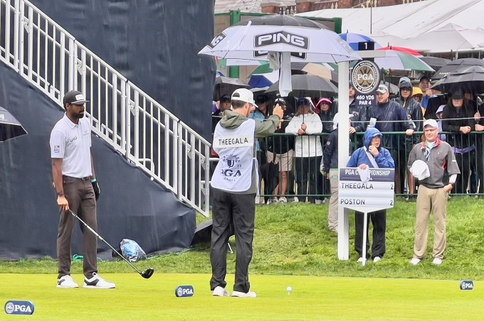 El caddie Carl Smith sostiene un paraguas para mantener su pelota seca mientras Sahith Theegala se prepara para jugar durante la tercera ronda del Campeonato de la PGA el 20 de mayo. Foto: Golfweek