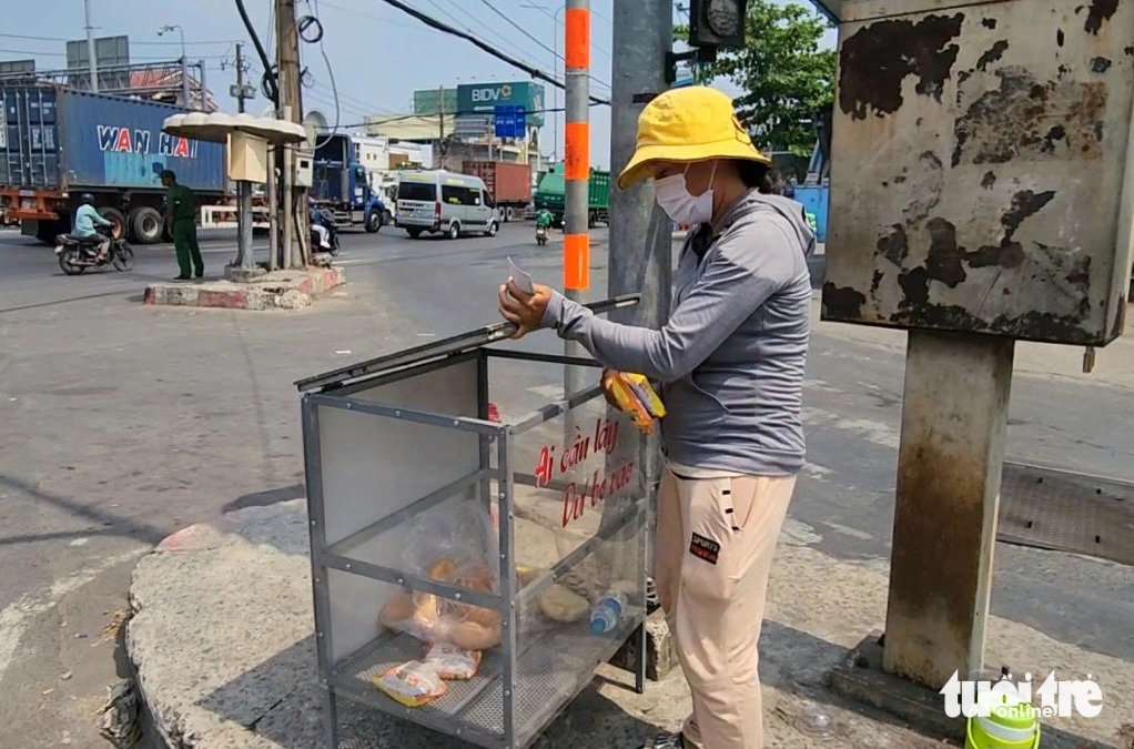  Trong lúc đi bán vé số dạo, chị Lâm Thị Thu Tuyết (quê Sóc Trăng) lấy hai gói mì trong chiếc tủ có dòng chữ 'ai cần lấy, dư bỏ vào' đặt gần đèn tín hiệu giao thông tại khu vực giao lộ Nguyễn Văn Bứa - quốc lộ 22 (huyện Hóc Môn) - Ảnh: NGỌC KHẢI