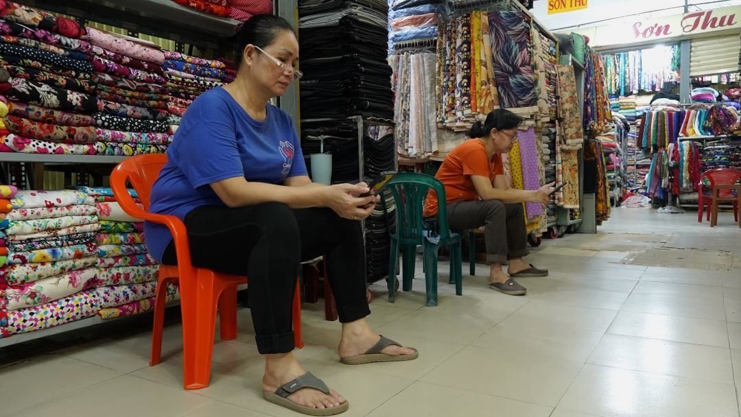 Sitzen und am Telefon surfen, chatten usw. ist für kleine Händler eine Möglichkeit, die Zeit totzuschlagen, um durch den Tag zu kommen. Foto: Yen Phuong