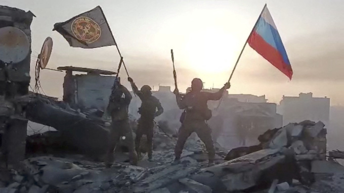 Members of the Wagner group raise a Russian flag and a Wagner flag over an undisclosed ruined building in a video released on May 20. Photo: Reuters