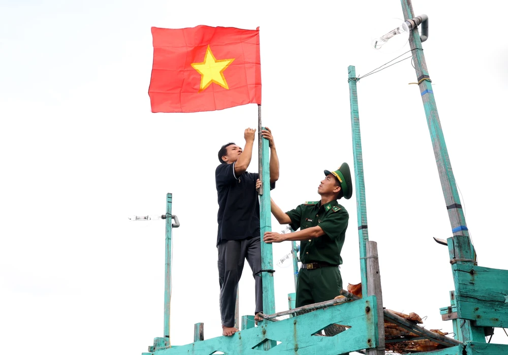 Los guardias fronterizos ayudan a los pescadores a colgar la bandera nacional en los barcos pesqueros. (Foto: Hong Dat/VNA)