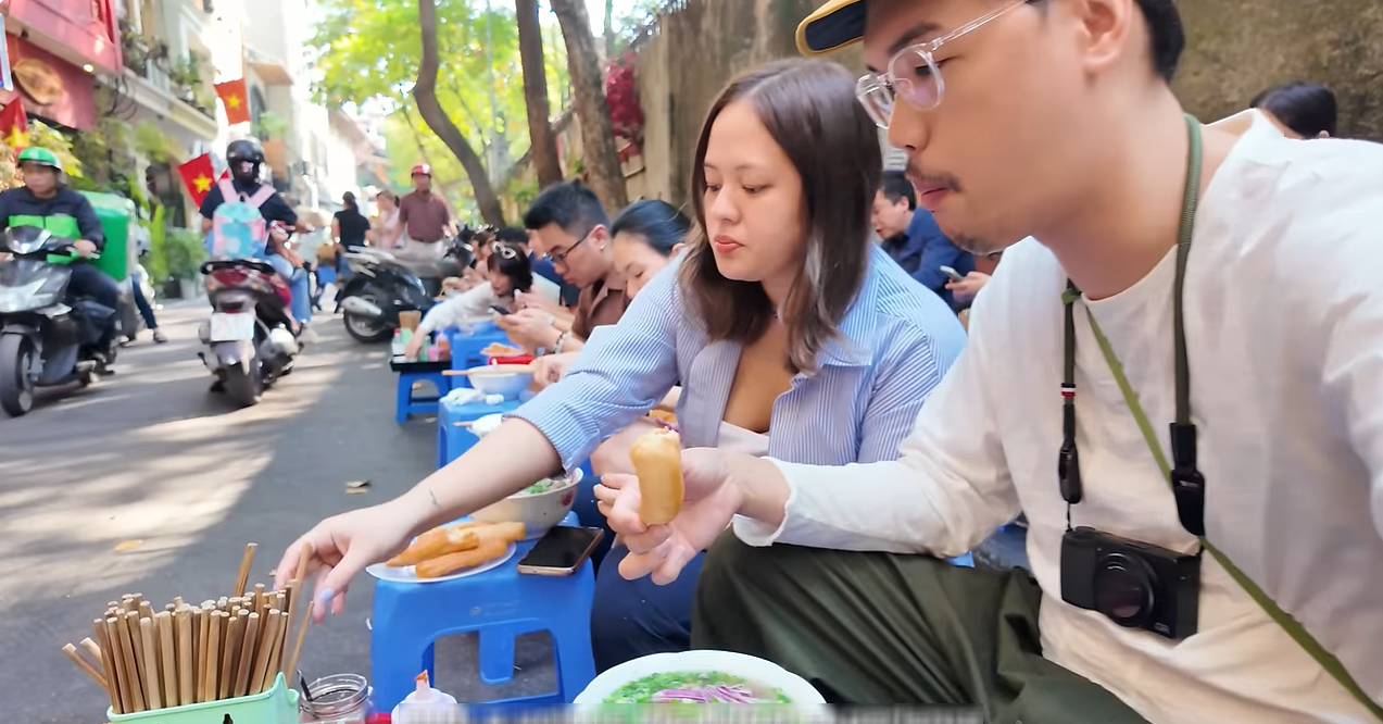 ハノイの歩道に座り、ミシュランのフォーを食べながら、その美味しさに感嘆する外国人観光客。