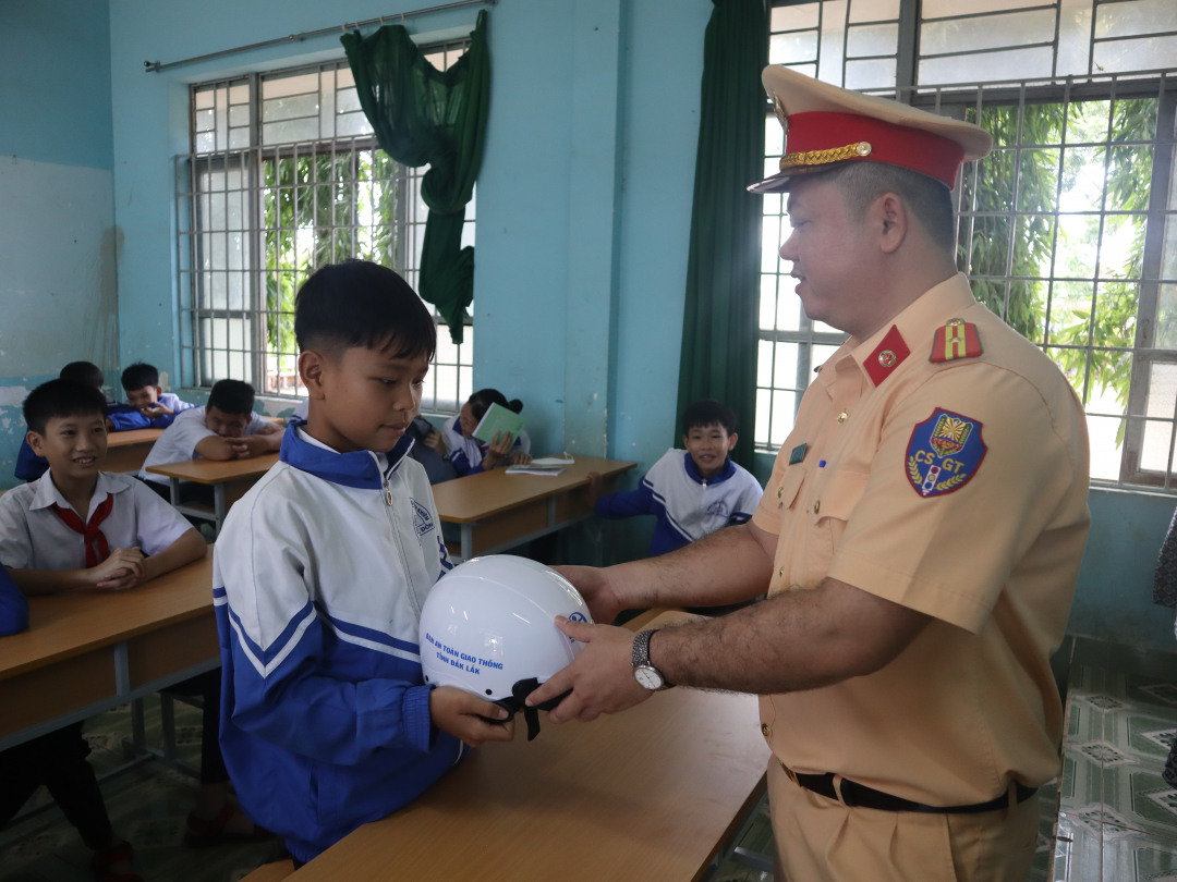 Oficiales del Equipo de Orden de la Policía de Tránsito, Policía del Distrito de Buon Don, entregan cascos a los estudiantes.