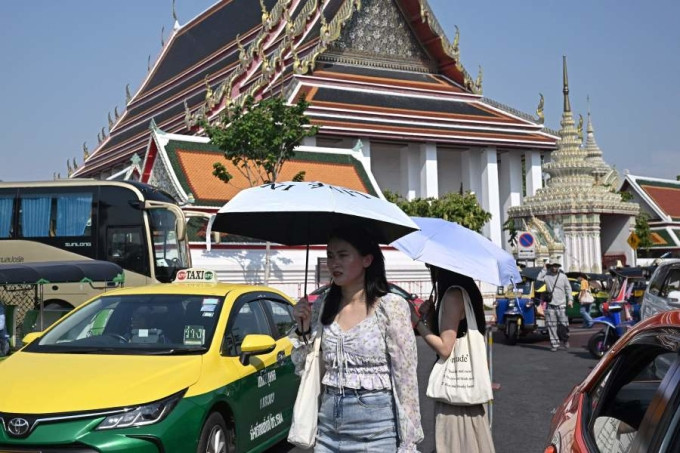 Touristen benutzen Regenschirme, um der Hitze zu entgehen, wenn sie Ende April den Wat Pho-Tempel in Bangkok besuchen. Foto: AFP