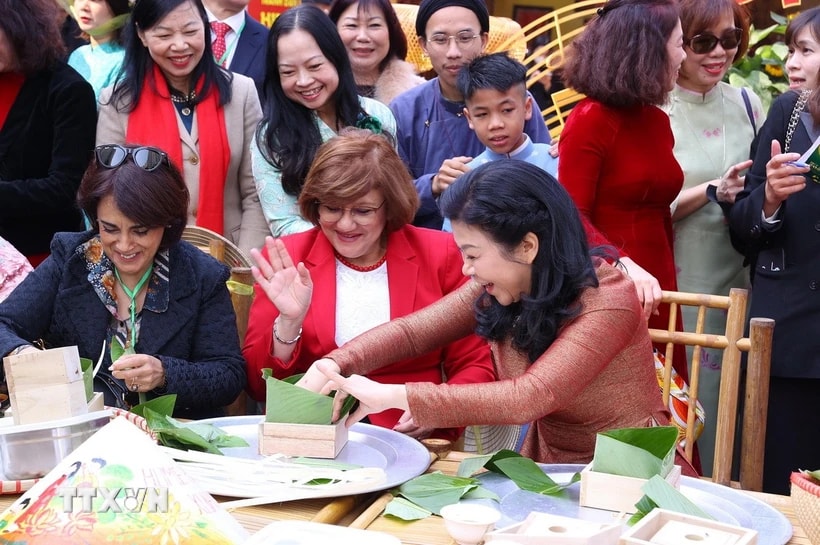 La Sra. Ngo Phuong Ly, esposa del Secretario General To Lam, y los delegados experimentan envolviendo y cocinando banh chung. (Foto: Van Diep/VNA)