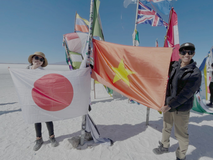 2023年冬、ボリビアのウユニ塩湖で両国の国旗の隣に立つ日本人とベトナム人のカップル。写真：キャラクター提供