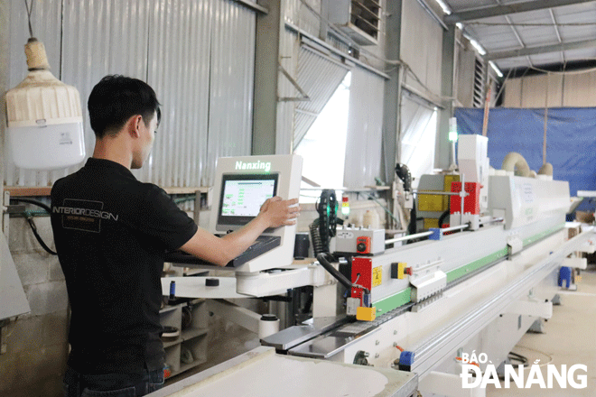 คนงานกำลังปฏิบัติงานเครื่องปิดขอบอัตโนมัติที่ P.A.D. บริษัท อาร์ต ดีไซน์ จำกัด  ภาพถ่าย: TRAN TRUC 