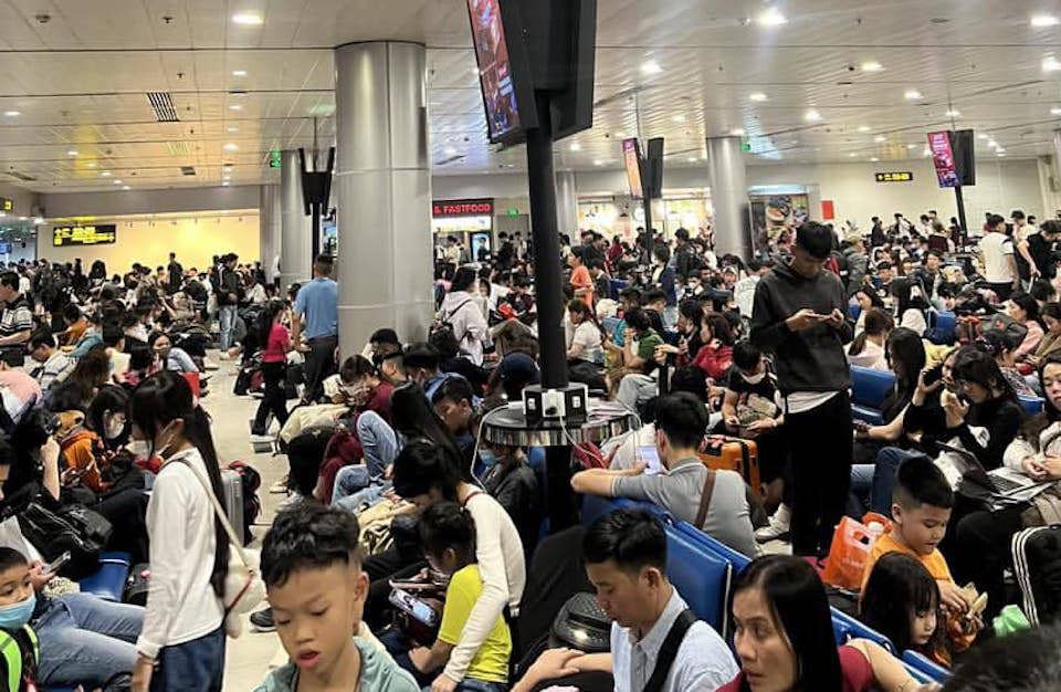 At the boarding gate area, there were many people waiting before the plane departed. There were not enough seats so many passengers had to stand or sit on the floor.