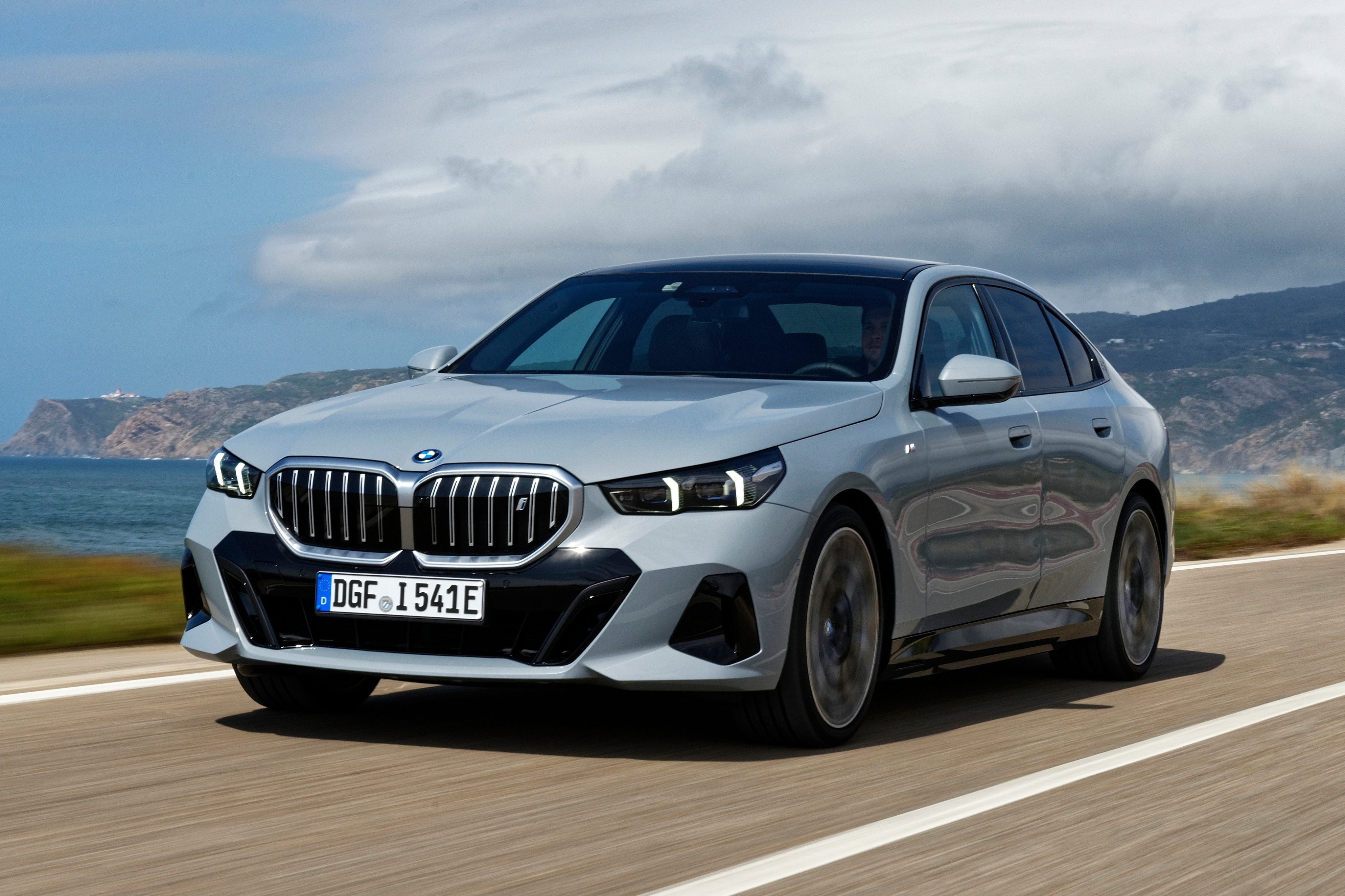 Der blaue BMW i5 fährt auf der Küstenstraße und zeigt das moderne Design des deutschen Autokonzerns.