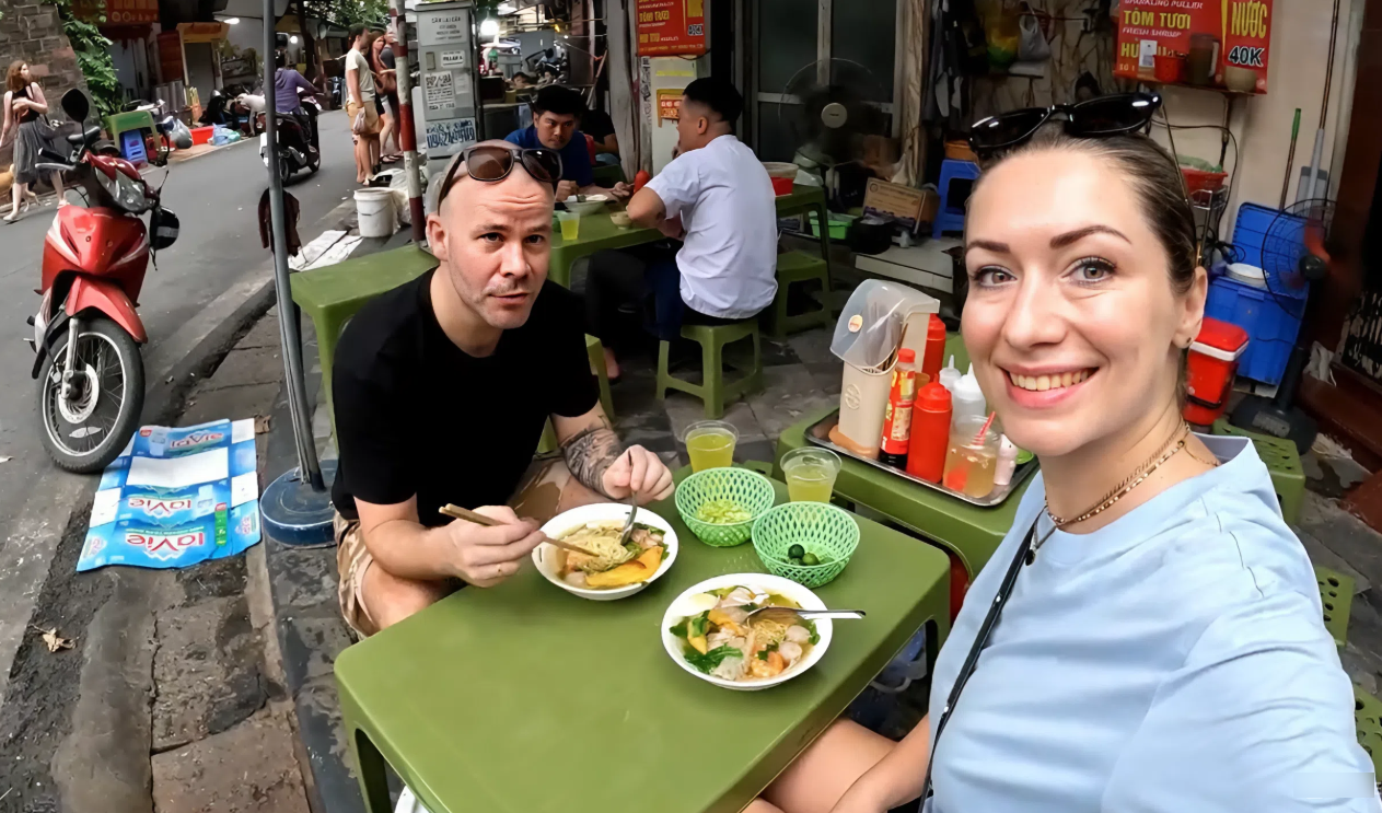 นักท่องเที่ยวชาวอังกฤษ 2 คนกำลังเพลิดเพลินกับบะหมี่เกี๊ยวที่ร้านอาหารริมถนนในฮานอย