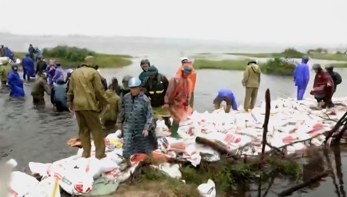 Hơn 100 người được huy động gia cố đê bao, ngăn nước tràn xuống khu dân cư. Ảnh: G.Hưng.