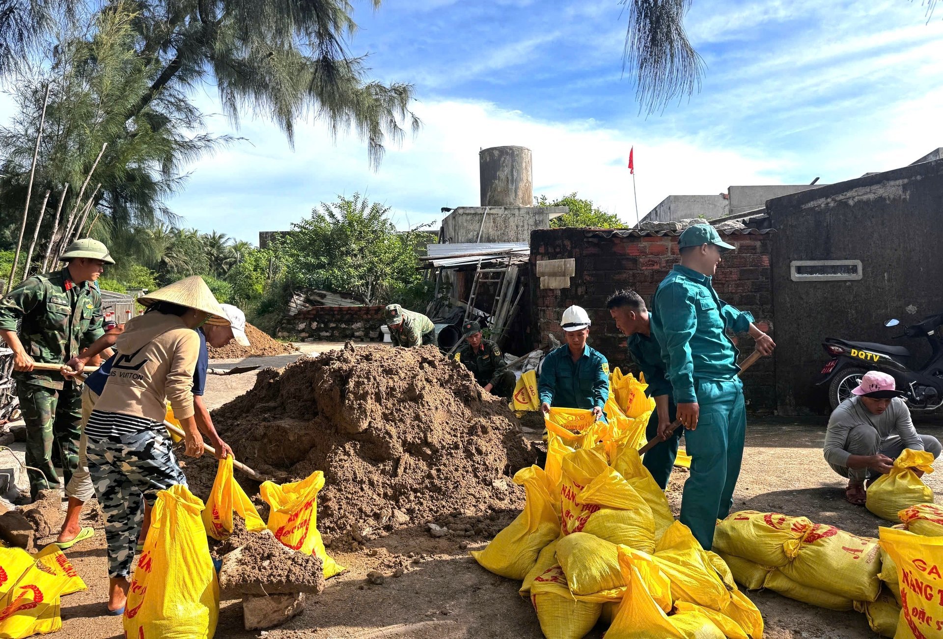 সৈন্য এবং শক ট্রুপরা নহন চাউ দ্বীপের লোকদের ছাদকে টেকসই করার জন্য ব্যাগে বালি ভরতে সাহায্য করছে। ছবি: অবদানকারী। Bộ đội và lực lượng xung kích giúp dân xã đảo Nhơn Châu cho cát vào bao để giằng mái nhà. Ảnh: CTV.