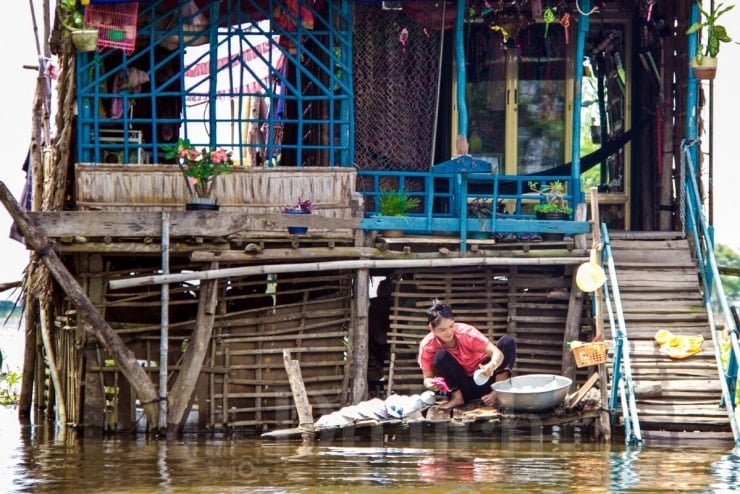 ដំបូលផ្ទះឈើឆ្កាងឆ្លុះលើទឹកហូរ ហើយនៅពីមុខរានហាលមានសំប៉ាន់ជាច្រើនបានបោះយុថ្កា ត្រៀមសម្រាប់ការនេសាទពេលព្រឹកព្រលឹម។