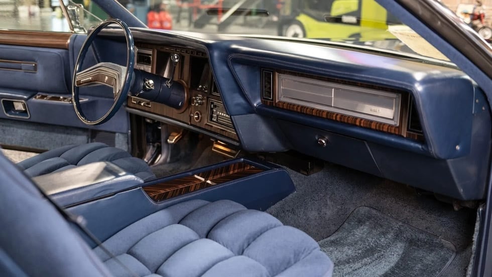 Interior sisi penumpang dengan dasbor biru, roda kemudi, dan jok berlapis tebal.