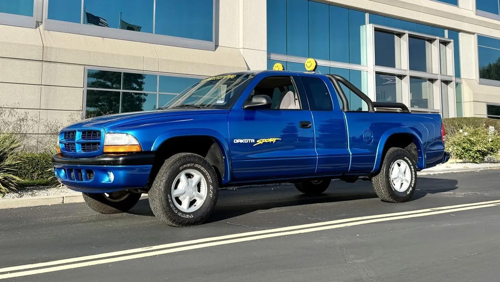 ជ្រុង​ខាង​ឆ្វេង​រថយន្ត​ភីកអាប់​ពណ៌​ខៀវ​ចត​នៅ​មុខ​អគារ​កញ្ចក់។