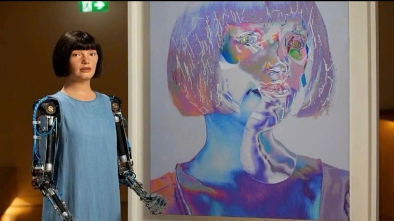 Robot humanoid bernama Ai-Da bersebelahan dengan potret diri yang dipamerkan di Galeri Seni Baharu di London.