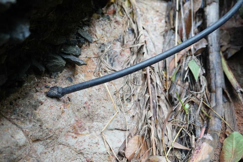 Một đoạn dây, trông giống như dây điện, bị đứt nằm dài theo mặt đường. Nếu là dây đang dẫn điện thì tiềm ẩn nguy cơ gây tai nạn điện cho người đi đường.