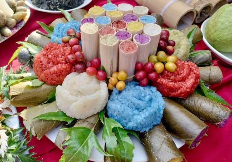 Muong-kvinna i traditionell dräkt bredvid dörren till ett hus på pålar, vilket visar ett unikt kulturellt särdrag.