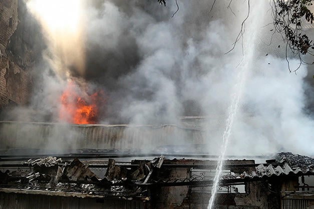 Anggota bomba menyembur air terus ke kawasan yang terbakar, dan asap putih tebal menyelimuti seluruh deretan bangunan. (Foto: VNA).