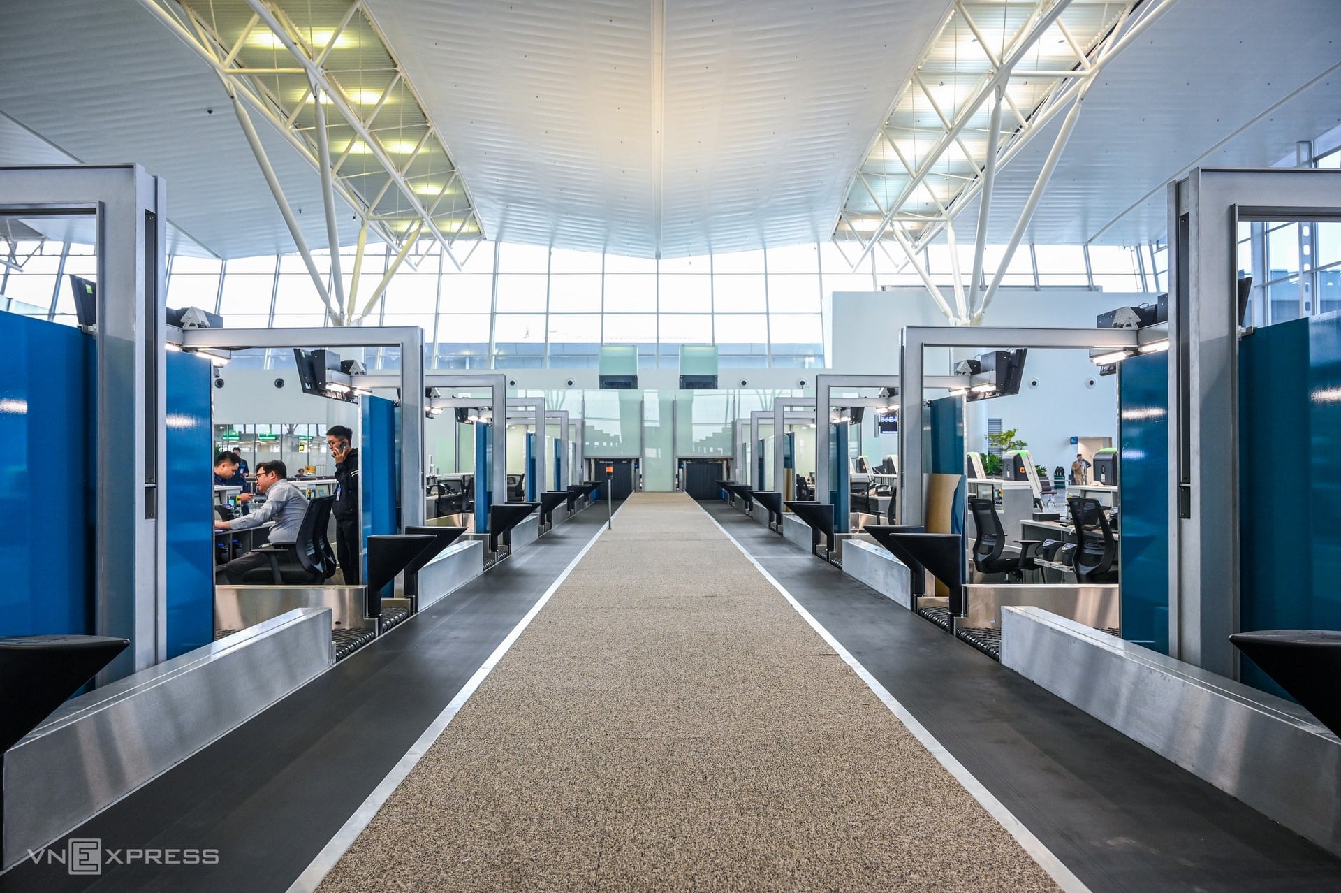 যাত্রীরা তাদের লাগেজ কনভেয়র বেল্টে রাখার সময় দেখছেন।