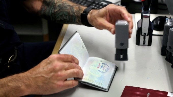 ເຈົ້າໜ້າທີ່ກວດຄົນເຂົ້າເມືອງກຳລັງປະທັບຕາໜັງສືຜ່ານແດນໃຫ້ນັກທ່ອງທ່ຽວ. ຮູບພາບ: NYT