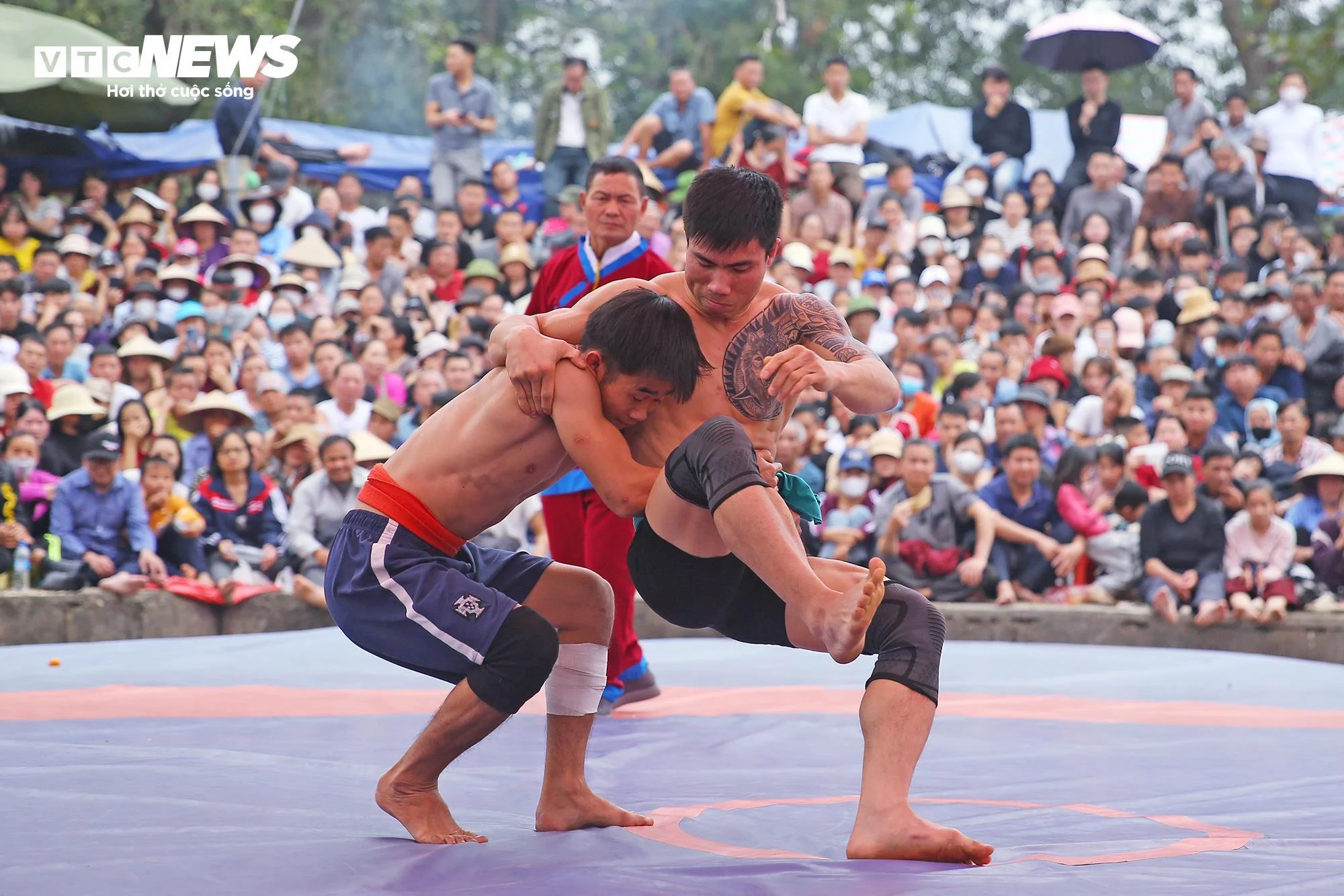 村の祭りで総合格闘技の名人が勝利、レスラーがバケツや袋を手にお金の「雨」を受け止める