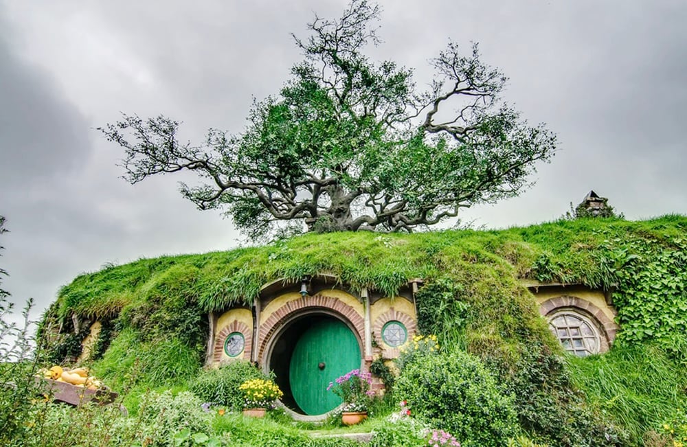 Sebuah rumah Hobbit yang terletak di lereng bukit, menampilkan pintu bundar yang khas dan dikelilingi oleh banyak bunga. Foto: H.Lam