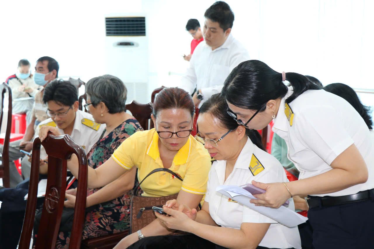 Cán bộ thuế hướng dẫn người dân cài đặt ứng dụng tại hội nghị.