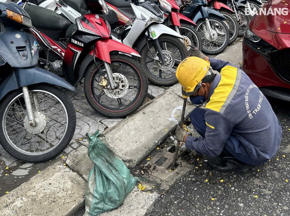 Công nhân Công ty Thoát nước và xử lý nước thải Đà Nẵng tranh thủ khơi thông cửa thu nước mưa vào chiều 11-6. Ảnh: H.H