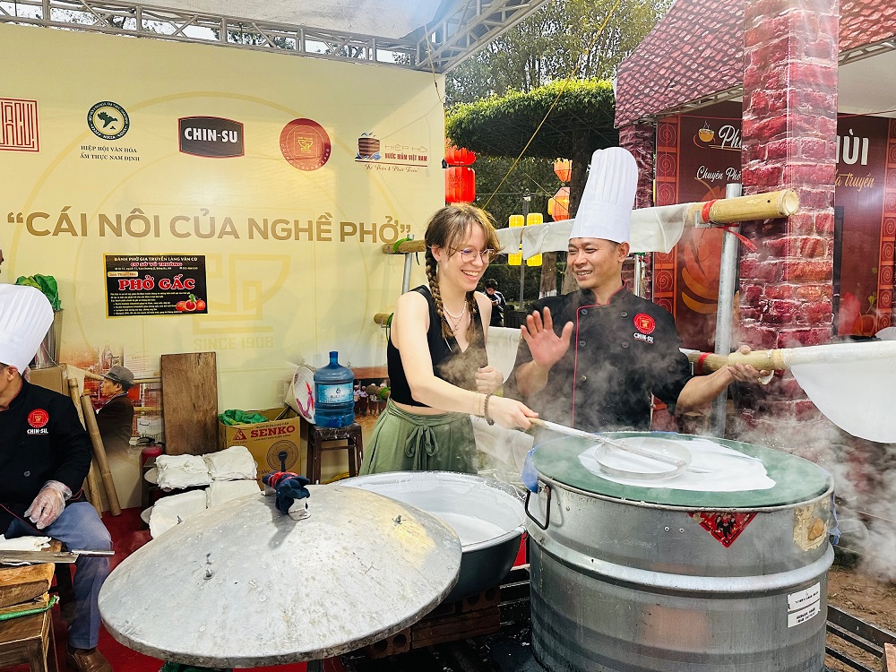 Du khách nước ngoài trải nghiệm tráng bánh phở tại gian hàng Chi hội Phở Vân Cù - Ảnh: Masan Group