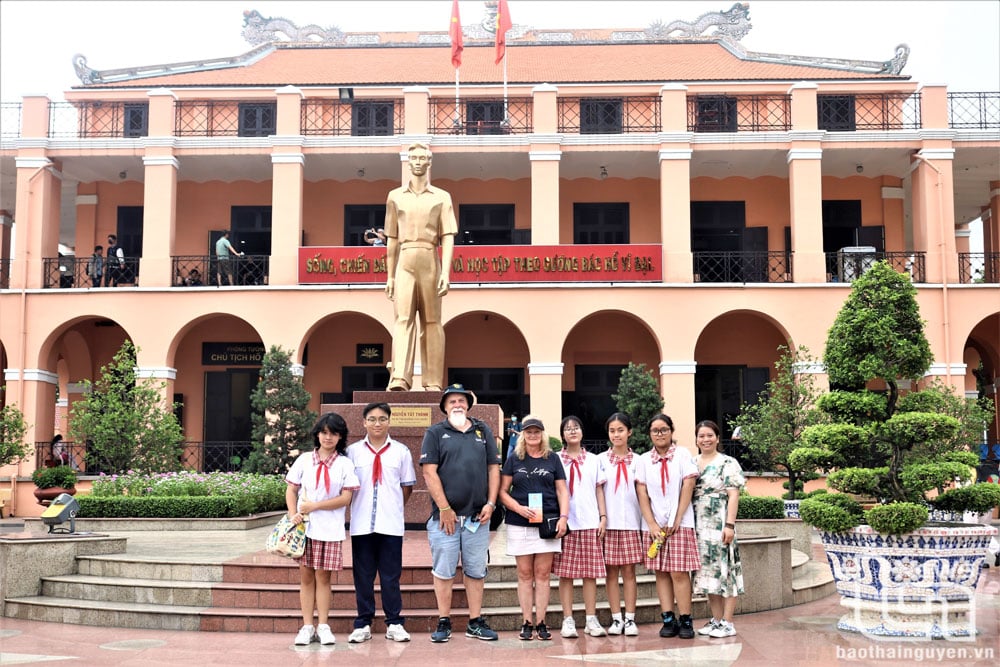 Du khách quốc tế chụp ảnh lưu niệm cùng học sinh dưới chân tượng đài người thanh niên yêu nước Nguyễn Tất Thành.