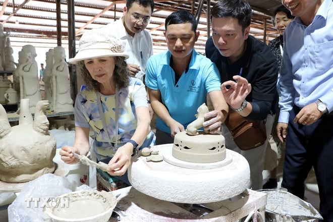 Các vị khách quốc tế trải nghiệm vẽ hoa văn lên các bình gốm thô. (Ảnh: Mạnh Tú/TTXVN)