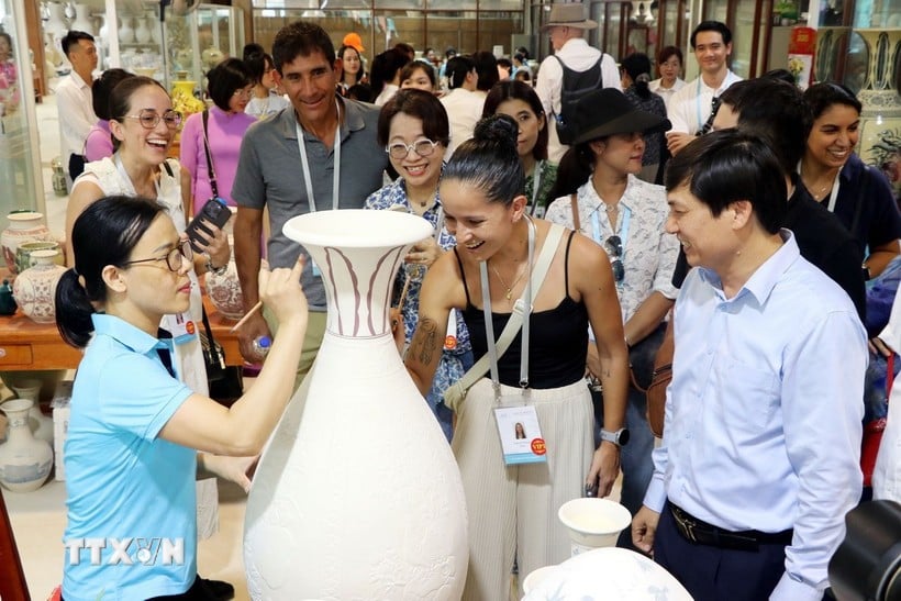 Các vị khách quốc tế trải nghiệm vẽ hoa văn lên các bình gốm thô. (Ảnh: Mạnh Tú/TTXVN)